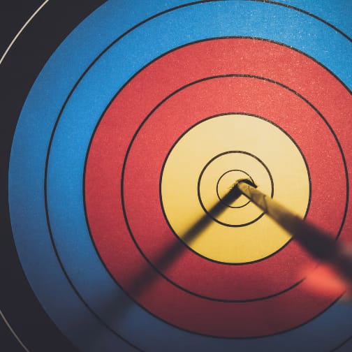 An archery target board with an arrow lodged into the center target.