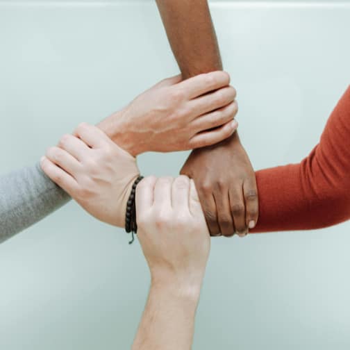 Four people holding each other's wrists in a supportive manner.